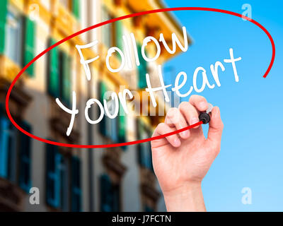 Hand des Mannes Follow Your Heart mit schwarzem Filzstift auf Bildschirm zu schreiben. Isoliert auf Stadt. Wirtschaft, Technologie, Internet-Konzept. Stock Foto Stockfoto