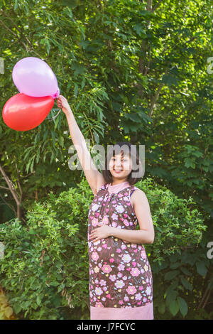 Schwangere Frau mit bunten Luftballons in den Sommerpark. Stockfoto