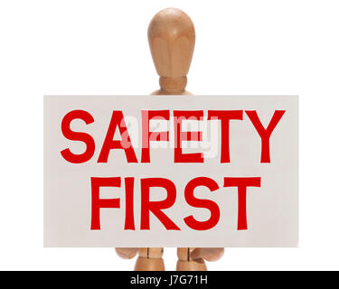 Hölzerne Puppe hielt eine weiße Karte mit der Meldung "Sicherheit erste" auf einem weißen Hintergrund Stockfoto