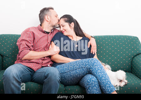Junger Mann küssen Girlfrined Stirn mit Liebe sitzend auf Sofa in der Nähe ihres Welpen Stockfoto