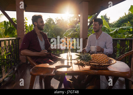 Zwei Mann sitzt auf der Sommerterrasse Hold Cup sprechen, Jungs Morgen trinken Kaffee im Freien zu frühstücken Stockfoto