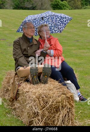 Ein älteres Paar teilen einen Regenschirm sitzend auf einem Ballen Heu in einem Feld in Schottland. Stockfoto