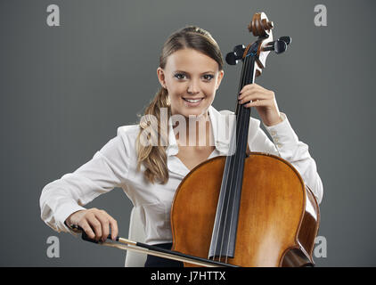 Lächelnde junge Frau Cellist auf grauem Hintergrund Stockfoto