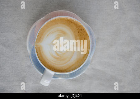 Käsekuchen mit Erdbeeren und Tasse Latte Kunst auf weiße Textur mit Blumen. Stockfoto