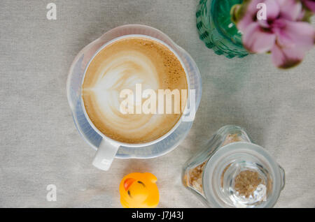 Käsekuchen mit Erdbeeren und Tasse Latte Kunst auf weiße Textur mit Blumen. Stockfoto