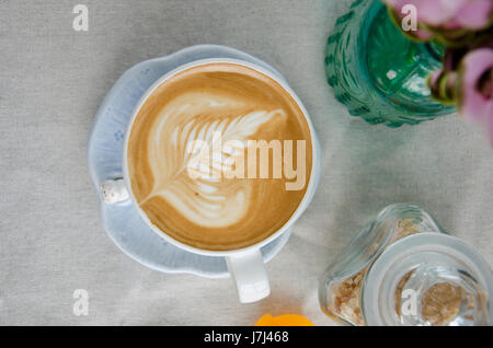 Käsekuchen mit Erdbeeren und Tasse Latte Kunst auf weiße Textur mit Blumen. Stockfoto