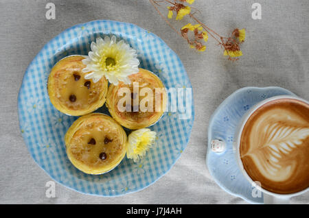 Käsekuchen mit Erdbeeren und Tasse Latte Kunst auf weiße Textur mit Blumen. Stockfoto