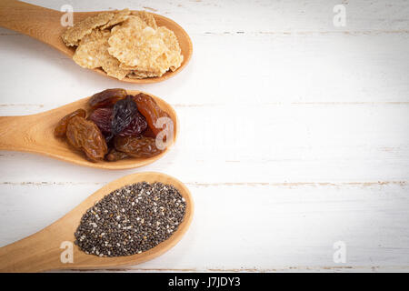 Satz von Rosinen, Vollkorn-Getreide-Flocken und Chiasamen in Kochlöffel auf weißem Holz Hintergrund. Stockfoto