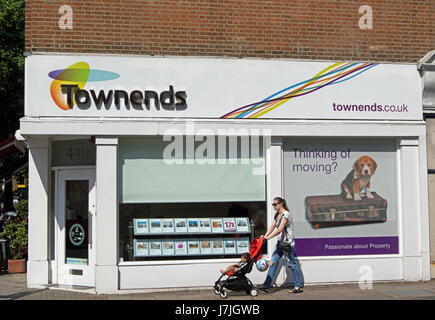 Frau mit Kind im Buggy, vorbei an einem Zweig von Immobilienmaklern, Townends in Chiswick, London, england Stockfoto