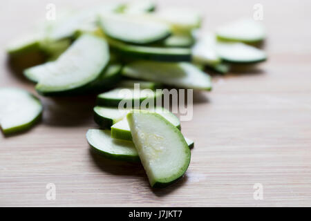 Dünne Scheiben Zucchini halb auf hölzernen Schnittfläche Stockfoto