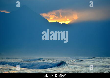 einsamer Surfer fast verloren in den riesigen Wellen der North Shore vor dem Hintergrund der West Maui Mountains Stockfoto