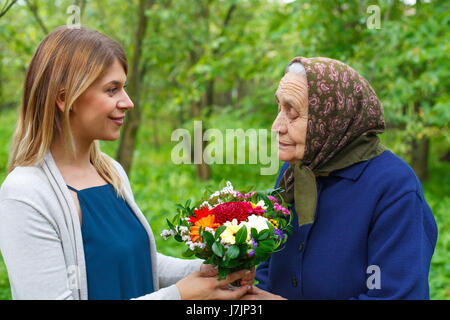 Glückliche alte Frau Blumen von ihrer Enkelin Stockfoto