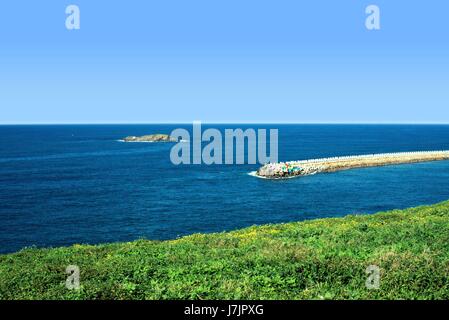 Bei strahlend blauem Himmel auf der Oberseite, dann blaue Meer Wasser und grünen Pflanzen an der Unterseite. In der Ferne im Meer ist ein Wellenbrecher und eine Insel. Australische Landschaft. Stockfoto