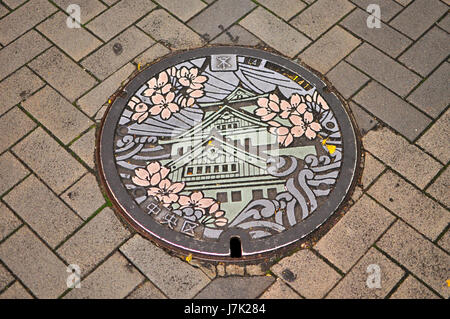 Eine Kanalisation Kanaldeckel in Kyoto, Japan, mit einem niedlichen und bunten Design eine japanische Burg und Sakura Blüten. Stockfoto