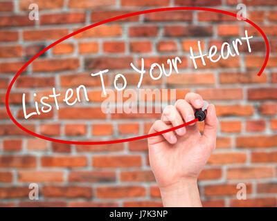 Hand des Mannes hören To Your Heart mit schwarzem Filzstift auf Bildschirm zu schreiben. Isoliert auf Ziegel. Wirtschaft, Technologie, Internet-Konzept. Stock Foto Stockfoto