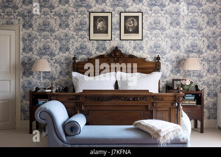Chaiselongue am Fuße des ein antikes Holz Bett im Schlafzimmer mit Toile De Jouy gemusterten Tapete Stockfoto