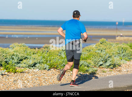 Mann joggt entlang einer Küstenstraße in Großbritannien. Stockfoto