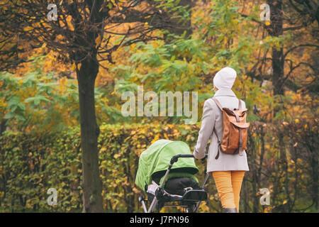 Junge Mutter schieben Kinderwagen im Herbst park Stockfoto