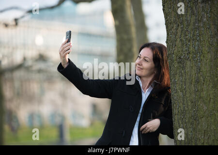 Business-Frau im schwarzen Anzug machen Selfies mit Smartphone stehen im park Stockfoto