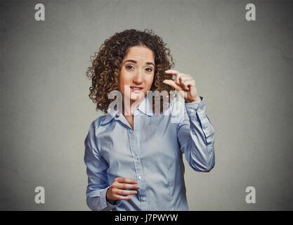 Closeup Portrait skeptisch jungen lockigen braunen Haaren Frau, die kleine Menge Geste mit der Hand die Finger isoliert graue Wand Background. Menschliche Emotionen fa Stockfoto