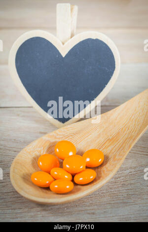 Orange Pillen in Holzlöffel mit leeren Herzen Form blackboard Stockfoto