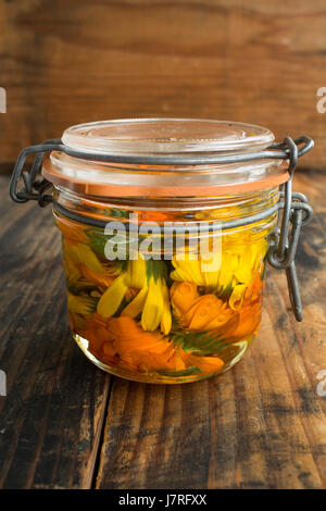 Calendula-Öl in einem Glas auf einem rustikalen hölzernen Hintergrund. Stockfoto