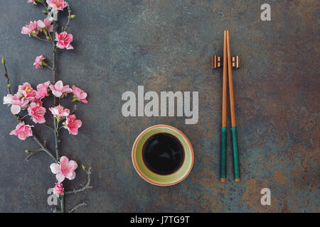 Sushi Set. Kleine Schale mit Sojasauce, Stäbchen und Kirschblüten, serviert auf Stein Hintergrund. Ansicht von oben, Leerzeichen Stockfoto
