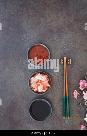 Sushi Set. Japanische Sushi-Stäbchen, Soja- und Chilisauce Bowl und eingelegtem Ingwer auf dunklen Stein Hintergrund Stockfoto