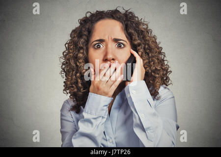 Kopfschuss schockiert betäubt junge Frau, die immer schlechte Nachrichten während des Gesprächs auf Handy isoliert graue Wand Hintergrund. Negativen menschliches Gesicht Ausdruck emot Stockfoto