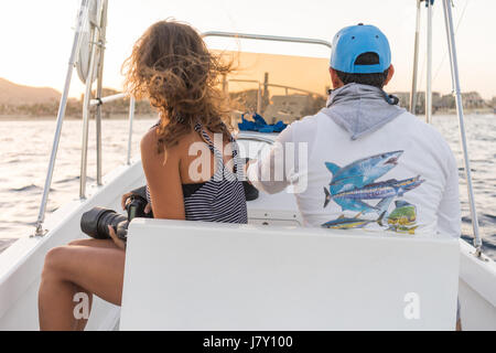 Junge Frau im Boot bei Sonnenuntergang in der Nähe von Felsformationen rund um den Bogen in Cabo San Lucas, Mexiko. Männlichen Fischer Boot fahren. Stockfoto