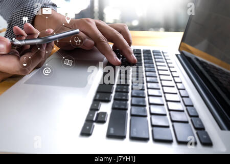 Mann mit Laptop zu Hause sitzend am Holztisch. Hände des Mannes auf dem Telefon eingeben Stockfoto