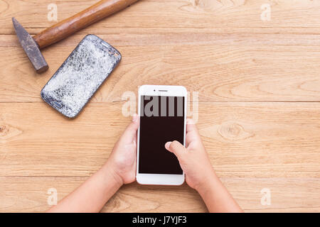 Ansicht von oben hand wählen neues Smartphone und brechen alte eins vom Hammer auf Holztisch Hintergrund Stockfoto