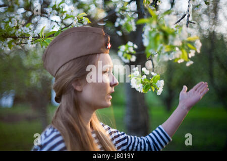 Mädchen in einem sowjetischen Kappe auf den Tag des Sieges in einem blühenden Garten Stockfoto