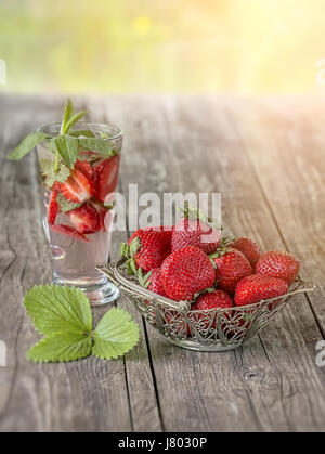 Erdbeere durchbrochenen Vase im Hintergrund des Glases mit einem Erdbeer Drink auf Holztisch an einem sonnigen Tag. Die vertikalen Rahmen. Stockfoto