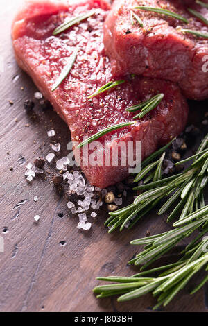 Rindersteaks mit Rosmarin, Salz und Pfeffer auf einem alten Holztisch. Stockfoto