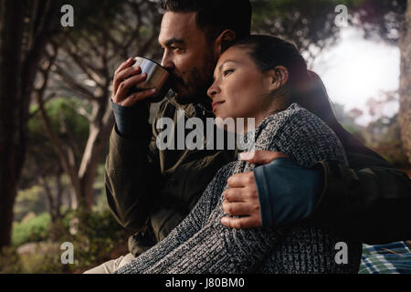 Junger Mann und Frau sitzen im Freien. Junges Paar ruht im Freien mit Mann trinkt Kaffee entspannt. Stockfoto