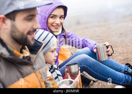 Seitenansicht des Lächelns Familie trinken heißen Tee von Metallschalen sitzen im freien Stockfoto