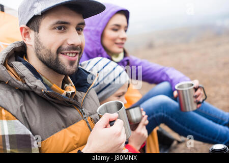 Seitenansicht des Lächelns Familie trinken heißen Tee von Metallschalen sitzen im freien Stockfoto