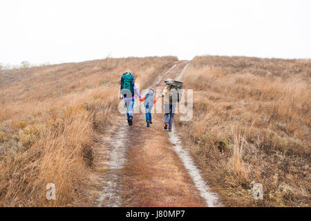 Rückansicht des jungen Familienglück mit Rucksäcken, Hand in Hand und läuft auf ländlichen Weg am trüben Herbsttag Stockfoto