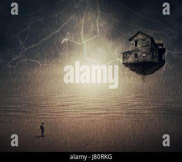 Surreale Backround eines Mannes im Regen vor einem fliegenden Haus Riss aus dem Boden, in der Nähe des Meeres stehen. Sixth Sense-Konzept. Stockfoto