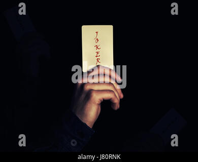 Nahaufnahme von einem Mann Hand hält Joker Spielkarte. Illusionist zeigt einen Zaubertrick auf einem schwarzen Hintergrund. Casino-Spiel-Konzept. Stockfoto