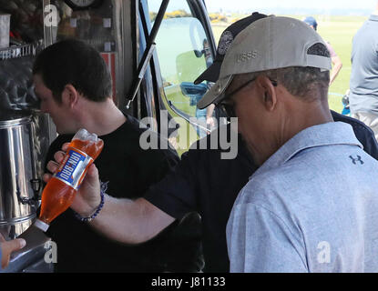 Sir Tom Hunter (teilweise verdeckt) zeigt dem ehemaligen US-Präsidenten Barack Obama eine Flasche Irn-Brus, während sie an einer Snackbar anhalten, während sie eine Runde Golf auf dem Old Course in St. Andrews, Fife, spielen. Stockfoto