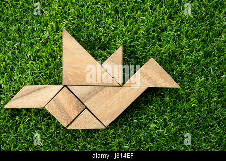 Hölzerne Tangram puzzle in fliegenden Vogel Form auf grünen Kunstrasen Hintergrund (Begriff der Freiheit, neue Erfahrung oder Unternehmer starten) Stockfoto