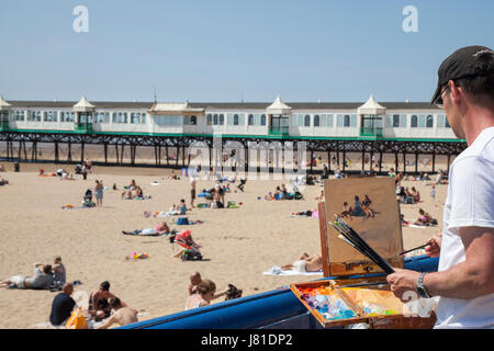 Lytham St Annes on Sea, Lancashire. UK Wetter. Landschaft Künstler Norman Lang" malt die Szene' an der Fylde Strand als Menschenmassen strömen zu den Pier und Resort Küste die Küste Sommer Sonnenschein in der Nähe von Blackpool zu genießen. Künstler des Jahres in Sieger 2013 Norman eröffnet seine erste London one man show, Leben in der Stadt, bei Osborne Studio Galerie. Diese ländliche Lancashire Küsten Edelstein, Lytham St. Anne's ist Sandstrand, der zu Hause reitet auf einem Esel, einem viktorianischen Pier und Kinderspielplätzen, nur der perfekte Ort, um die Essenz des Britischen Badeort zu erfassen. Kredit; MediaWorldImages/AlamyLivenews Stockfoto