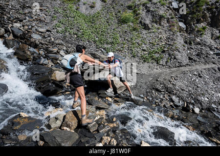 junger Mann hilft einer Frau, die Überquerung eines kleinen Baches am Berg, Alpen, Frankreich Stockfoto