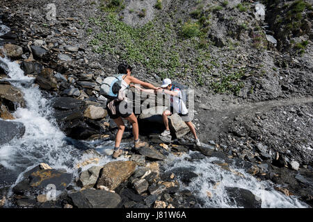 junger Mann hilft einer Frau, die Überquerung eines kleinen Baches am Berg, Alpen, Frankreich Stockfoto