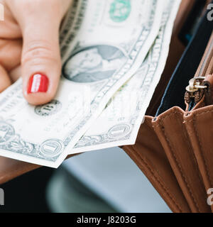 Das Mädchen Hand nimmt Papier-Dollar aus einer orange Leder Geldbörse. Krise und Wirtschaft-Konzept. Close-up. Stockfoto