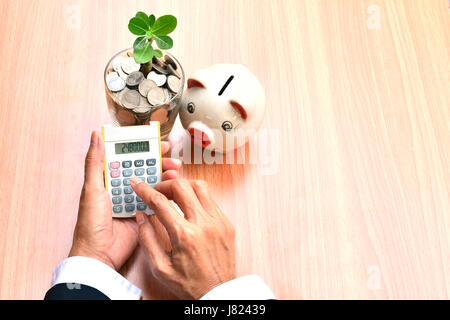 Finanzen, Hand der Person, die mit Taschenrechner mit Münzen in Glas und weißen piggy Bank Stockfoto