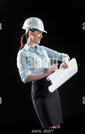 Architektin im Helm holding Blaupause und Armbanduhr schaute lächelnd Stockfoto
