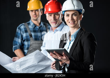 Zwei Architekten mit digital-Tablette und Blaupause und Ingenieur Blick in die Kamera und lächelnd Stockfoto